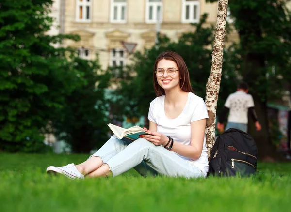 Улыбающаяся студентка в городском парке с книгой — стоковое фото