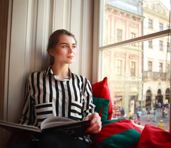 Evde kitap ile cam kenarında oturan kız öğrenci — Stok fotoğraf