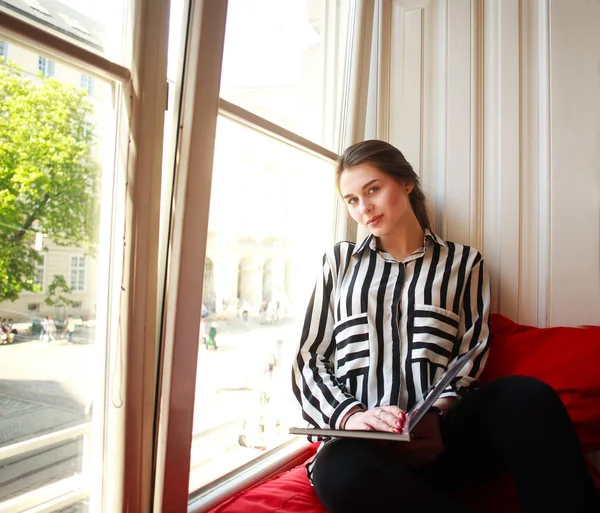 Flicka student sitter hemma vid fönstret med bok — Stockfoto