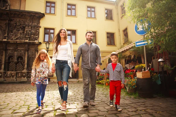 上の子供を持つ若い家族が観光都市の通りを歩く — ストック写真