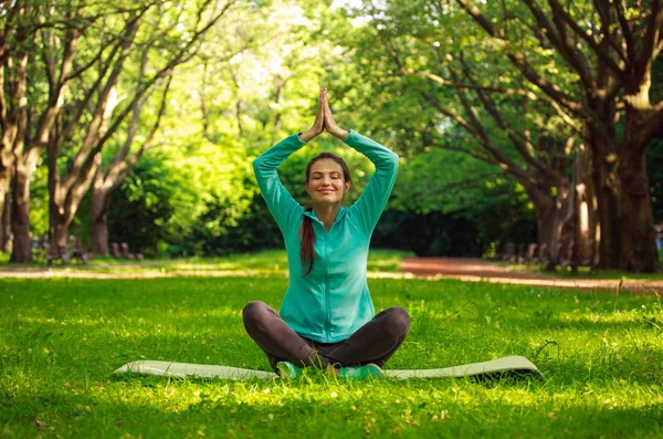 Jonge vrouw in zomer park doen yoga met gesloten ogen — Stockfoto