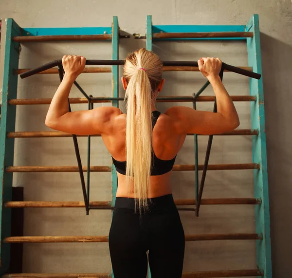 Sportieve atleet vrouw uitoefening pull-ups in sportschool doen vanaf achterkant — Stockfoto