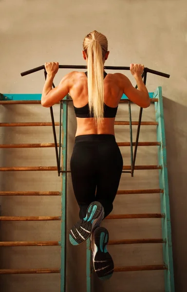 Sportieve atleet vrouw uitoefening pull-ups in sportschool doen vanaf achterkant — Stockfoto