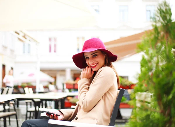 Elegancki, młoda kobieta w ulicznej kawiarni z telefonu na tle miasta — Zdjęcie stockowe