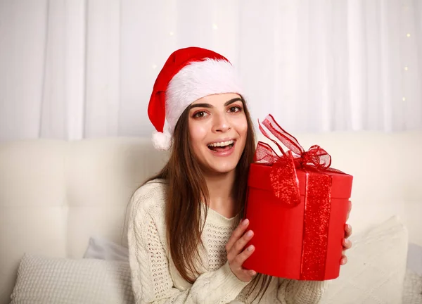 Happy usmívající se žena v červené vánoční čepice s darem na posteli — Stock fotografie