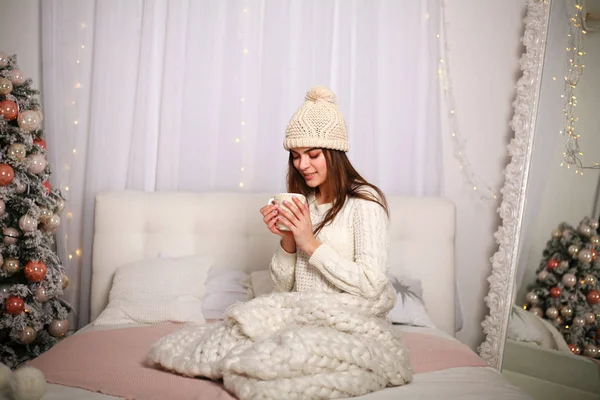 Девушка в зимнем свитере и шляпе в теплом одеяле дома на кровати — стоковое фото