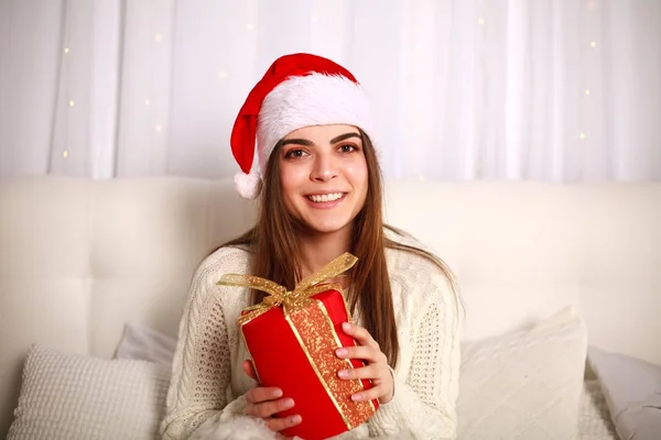 Happy usmívající se žena v červené vánoční čepice s darem na posteli — Stock fotografie
