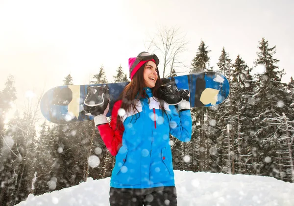 Smiling snowboarder girl in winter in snowfall on pine forest — Stock Photo, Image