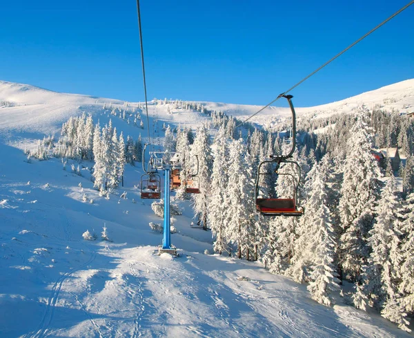 Skiliften in besneeuwde bergen en vuren bos op blauwe hemel — Stockfoto