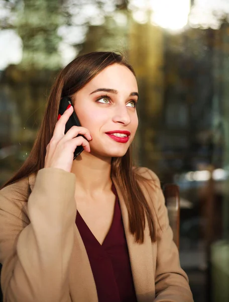 Linda chica de abrigo utiliza el teléfono móvil en la cafetería de verano —  Fotos de Stock