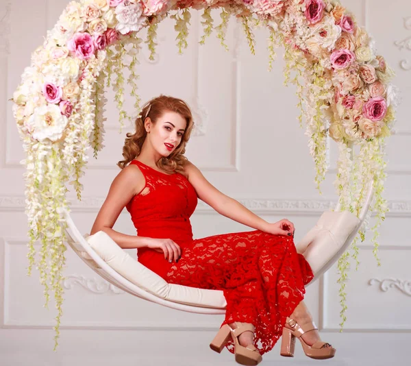 Mujer alegre elegante en vestido rojo en swing en flores —  Fotos de Stock