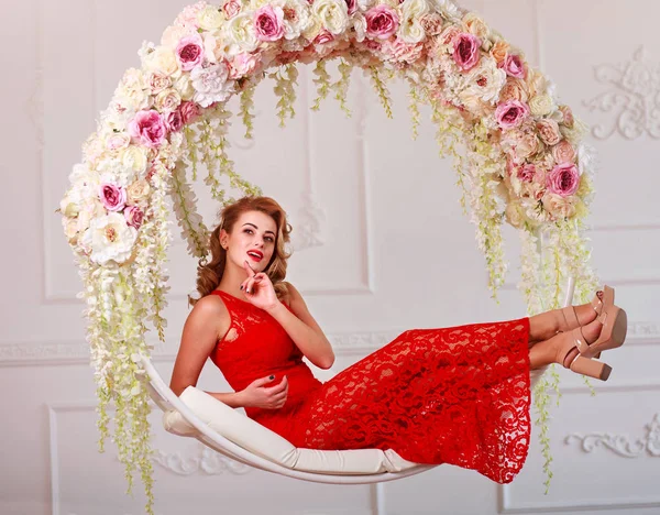 Радостная элегантная женщина в красном платье на качелях в цветах — стоковое фото