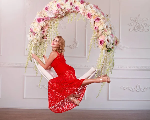 Joyful elegant kvinna i röd klänning på swing i blommor — Stockfoto