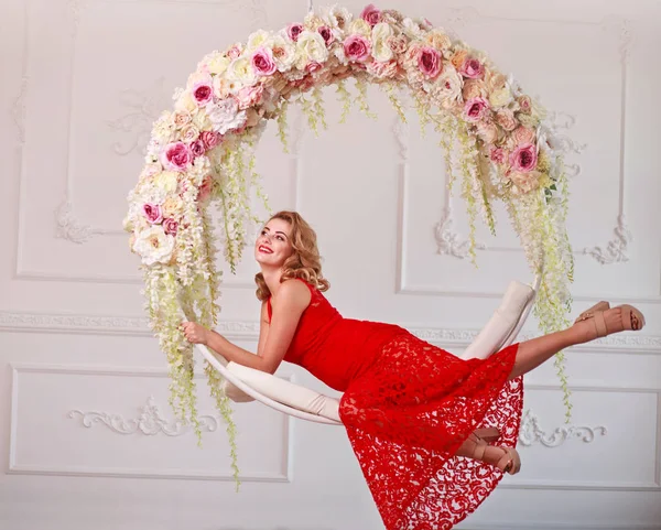 Freudig elegante Frau im roten Kleid auf Schaukel in Blumen — Stockfoto