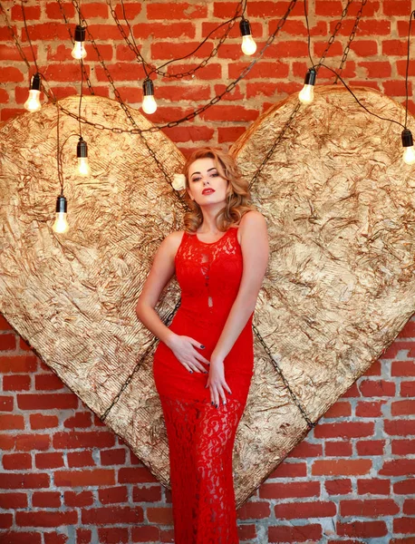Okouzlující žena v červených šatech na zlaté srdce ve studiu — Stock fotografie