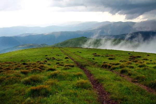 Route vers le champ au sommet des montagnes dans les nuages sur le ciel — Photo