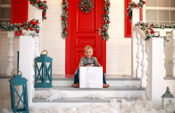 Маленький мальчик ребенок с подарком во дворе дома в рождественском декоре — стоковое фото