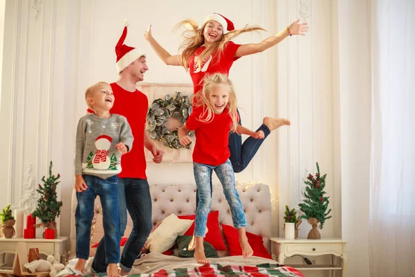 Счастливая молодая семья прыгает и веселится дома в постели на Рождество — стоковое фото