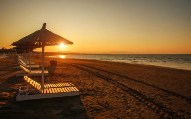 Karadağ 'da gün batımında deniz kenarındaki boş kumsalda güneşli yataklar