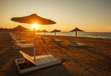 Karadağ 'da gün batımında deniz kenarındaki boş kumsalda güneşli yataklar