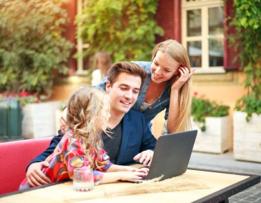 Genç bir aile kızlarıyla birlikte dizüstü bilgisayara bakıyor. 