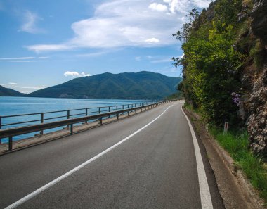 Deniz körfezi boyunca asfalt yol ve mavi gökyüzünde dağlar, Avrupa