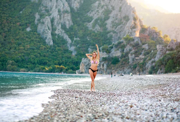 緑の山々を背景に地中海の小石のビーチで素敵な若い女性 — ストック写真