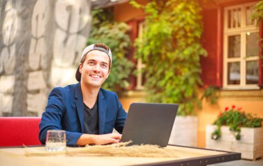 Yazlık bir kafenin avlusunda laptopun başında kep takmış yakışıklı bir iş adamı.