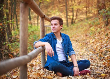 Orman parkındaki genç düşünceli ve hayalperest adam rahatlamanın ve doğanın tazeliğinin tadını çıkarıyor.