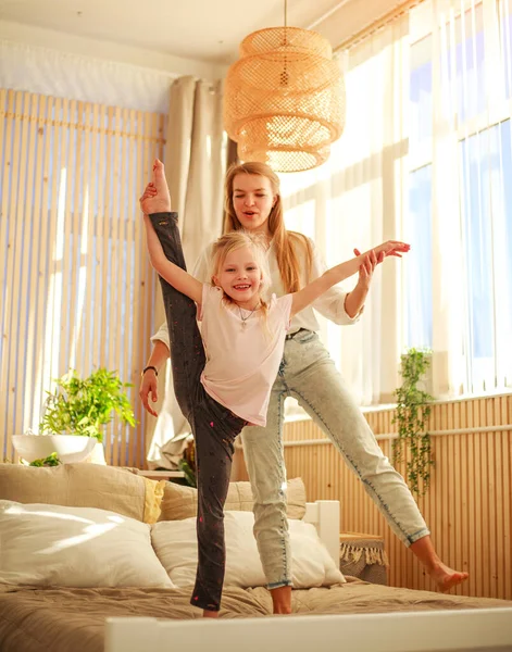 Mother and daughter on the bed at home jump, have fun, do acrobatic exercises, healthy leisure activity