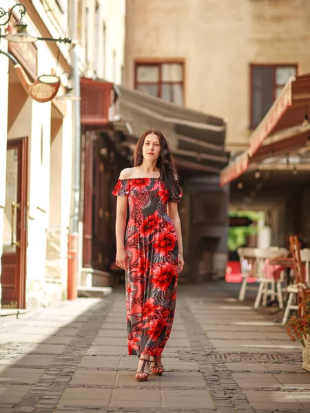 古いヨーロッパの町の通りに長いカラフルなドレスで官能的な魅力的な若い女性は花と散歩をお楽しみください — ストック写真