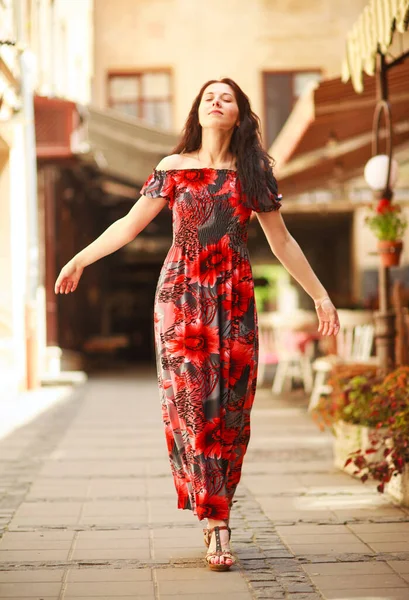 古いヨーロッパの町の通りに長いカラフルなドレスで官能的な魅力的な若い女性は花と散歩をお楽しみください — ストック写真