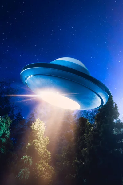Citra kontras tinggi UFO terbang di atas hutan dengan sinar cahaya di malam hari Stok Foto