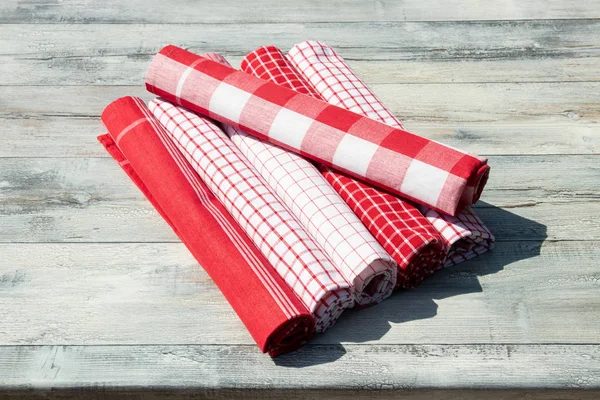 Stack van opgerolde rood wit geruite en gestreept linnen bedrukt op rustieke lichte houten tafel. Buiten. — Stockfoto