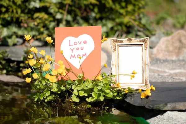 Self made card with white heart on red background and an empty vintage picture frame. On card is written Love You Mom.  Concept Mothers day.  Outdoor — Stock Photo, Image