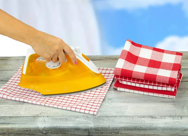 Woman ironing tablecloths on rustic grey table with a blue white background. Next to it is a pile of already ironed tablecloths. — Stock Photo, Image