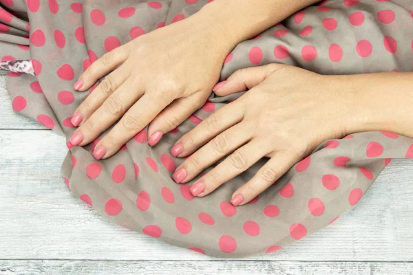 女人手上的粉红色修剪指甲拿着粉红色的美丽的围巾。背景是一张质朴明亮的桌子。概念美。特写. — 图库照片