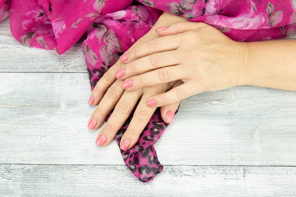 Женские руки розовый маникюр на ногтях, держа розовый красивый шарф. Фон - это деревенский светлый стол. Концепция красоты. Крупный план . — стоковое фото