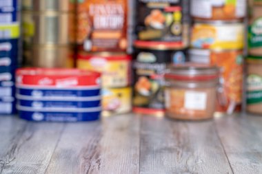 Coronavirus outbreak. Blurred image of stack of canned foods with a long shelf life such as fish, vegetables and meat stew, sausages and other goods on a table. Purchases in fear of coronavirus. clipart