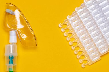 Coronavirus tedavisi konsepti. Solunum yolunun tedavisi için tıbbi yüz maskesi ya da nebulizatörü ve sarı arka planda düzleştirilmiş onlarca ampul paketi. Boşluğu kopyala.