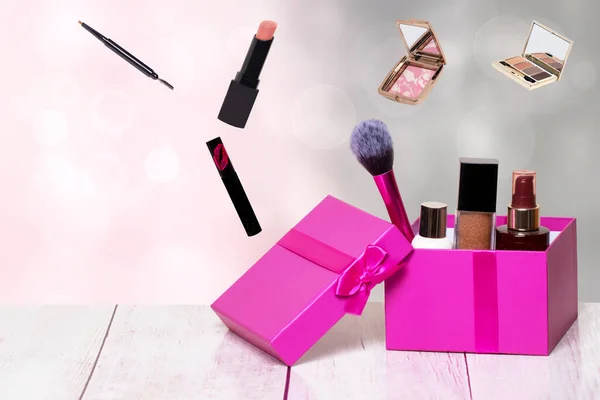 Decorative composition of colorful beauty and makeup products and tools in a pink gift box on a bright table and with further cosmetics accessories on a abstract background. Copy space for advertising on left side.