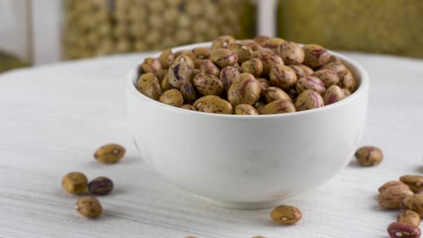 Dry pinto beans in white ceramic bowl. Spilled beans. — Stock Video