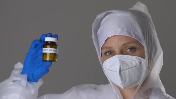 Viroloog in masker en beschermend pak met witte pillen in de hand. — Stockvideo