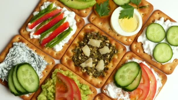 Deliciosas galletas saladas con salsa de queso, hummus, aguacate, pesto y verduras . — Vídeo de stock