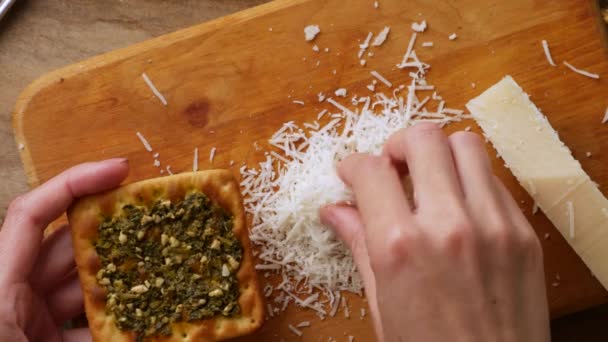 Vrouw hand bestrooi geraspte oude parmezaanse cracker met pesto. — Stockvideo