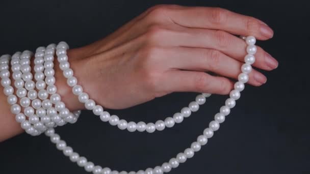 Mano di una donna che tiene la collana di perle bianche su sfondo grigio . — Video Stock