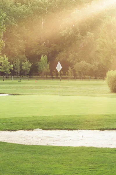 White flag on golf course with sun rays
