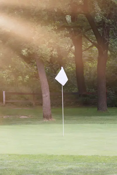 Campo de golfe com bandeira branca e raios de sol — Fotografia de Stock