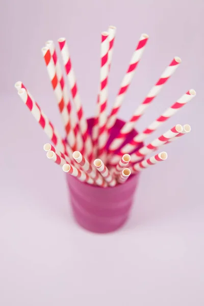 Bunte Strohhalme im lila Plastikbecher auf dem rosafarbenen Backgr — Stockfoto