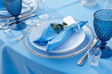 Restoranda mavi bir masa örtüsü üzerinde çatal bıçak takımı.